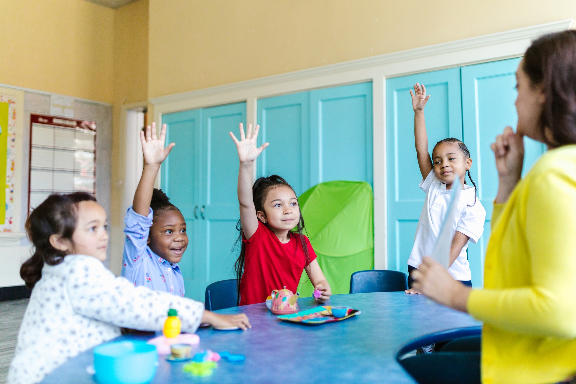 Group of students raise their hands around a table as they work on subtraction activities.