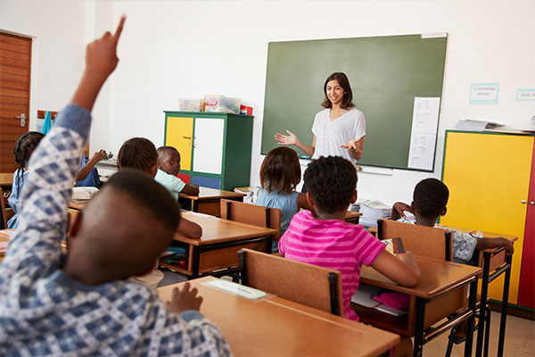 The teacher is waiting for answers for her question while a student rise his hand