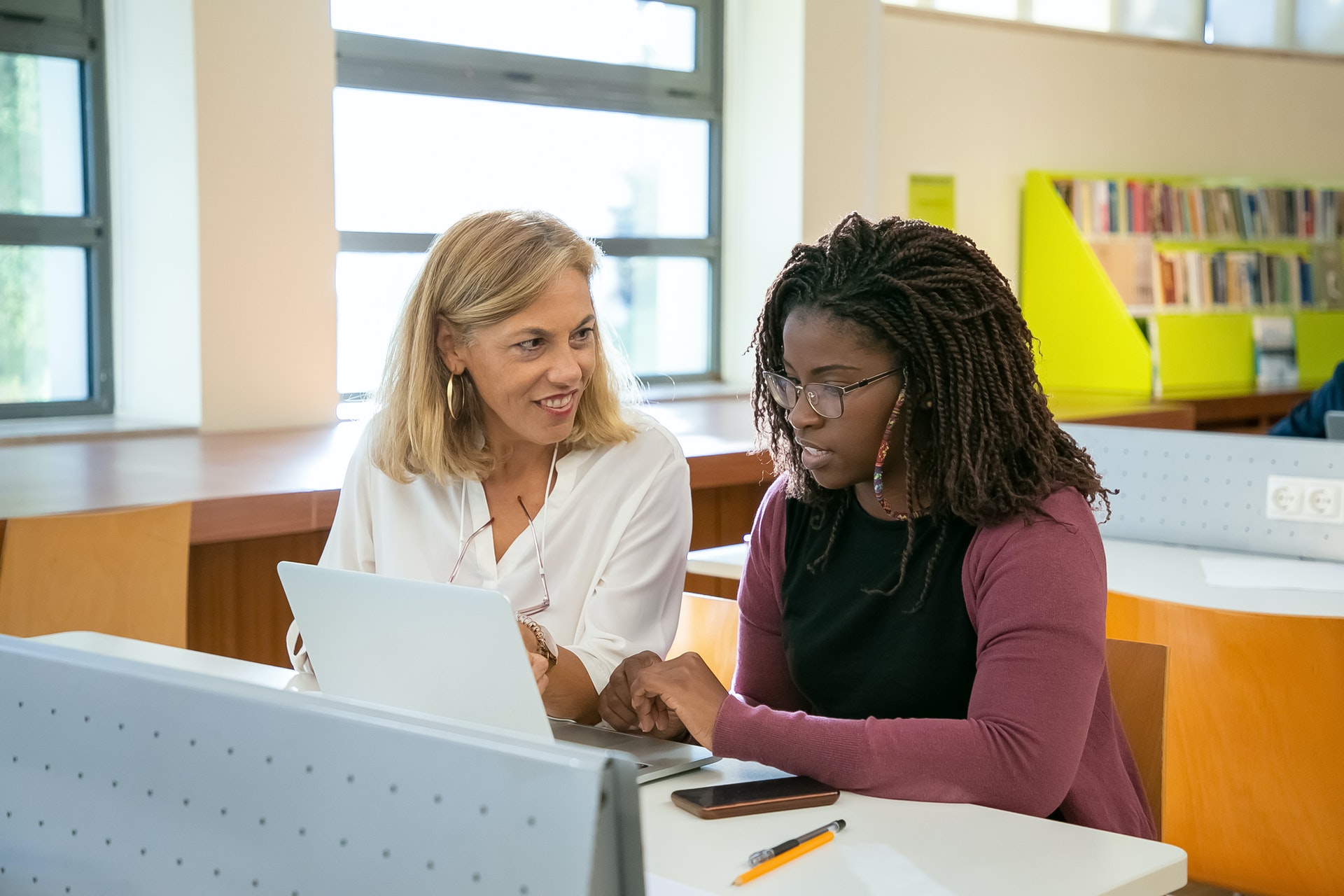 Two teachers sit in a classroom and look at a classroom website on a laptop computer.