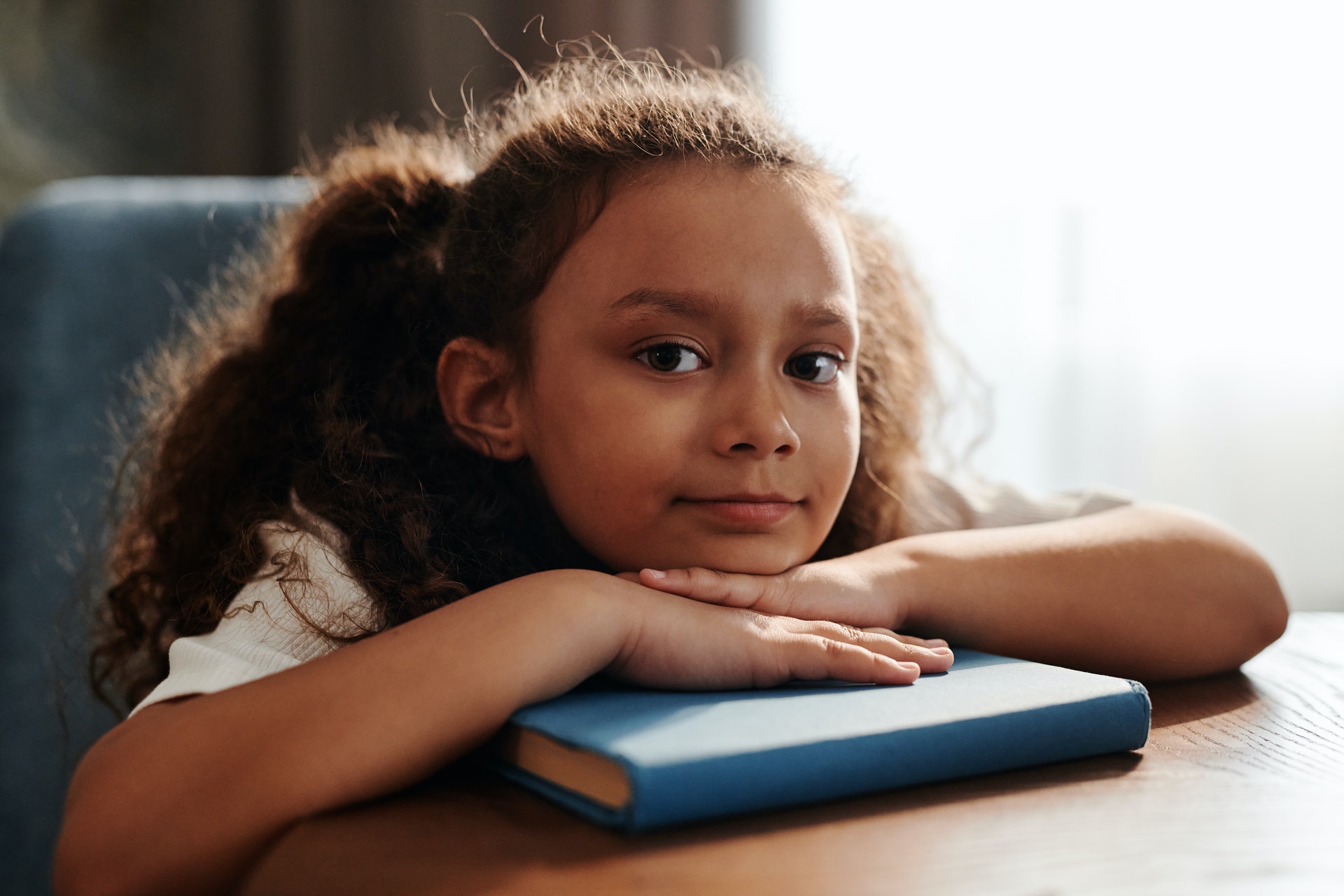Young girl rests her head on a book and looks into the camera.